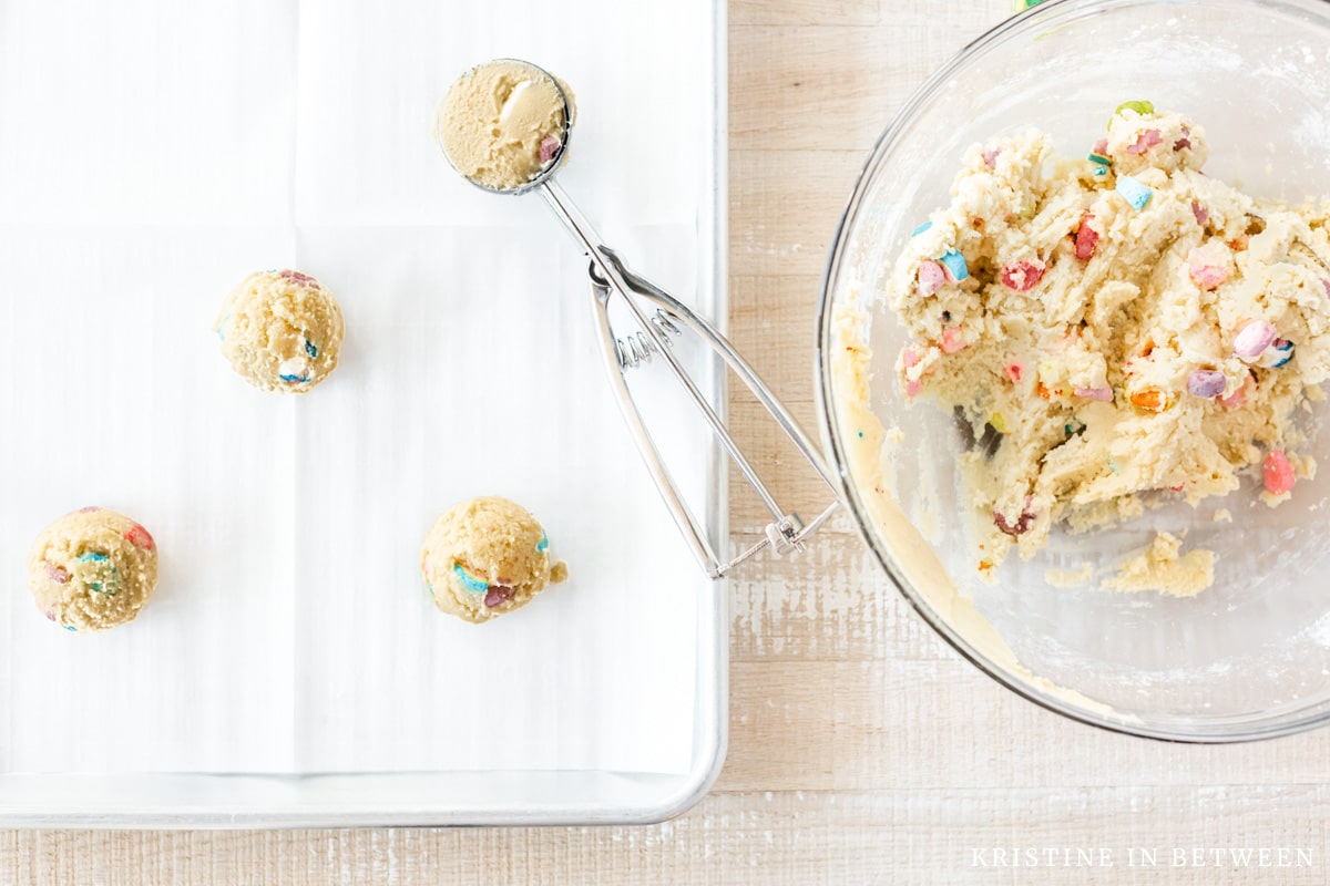 Scooped cookie dough on an aluminum baking sheet with a cookie scoop.