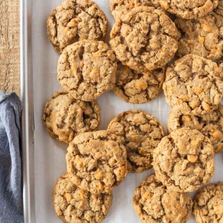 Butterscotch oatmeal cookies laying on a baking sheet with a blue napkin next to them.