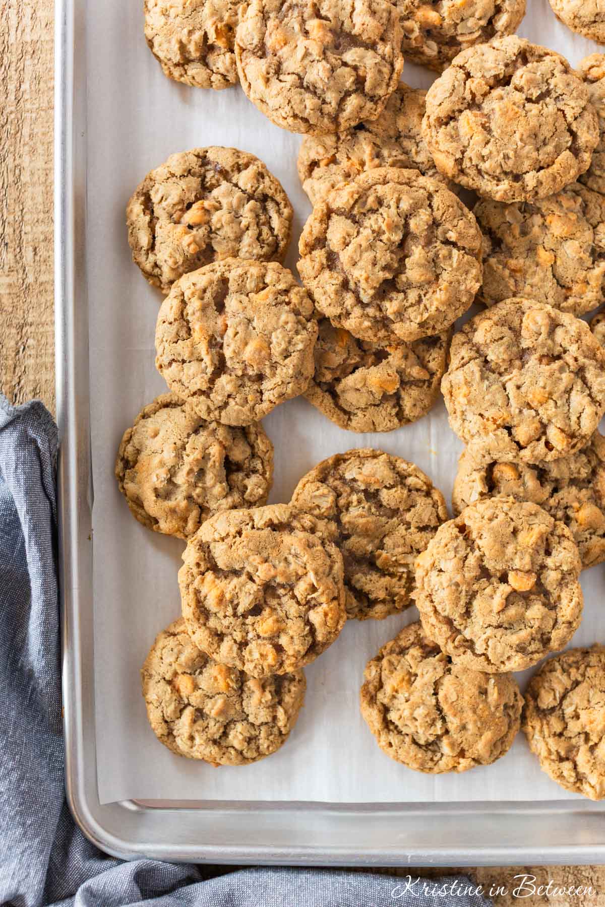 Butterscotch oatmeal cookies laying on a baking sheet with a blue napkin next to them.