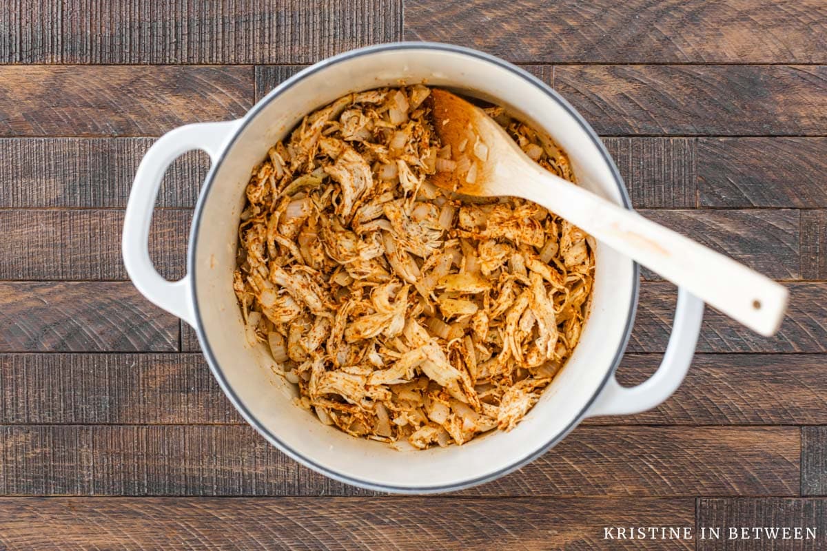Shredded chicken covered in spices in a Dutch oven with a wooden spoon.