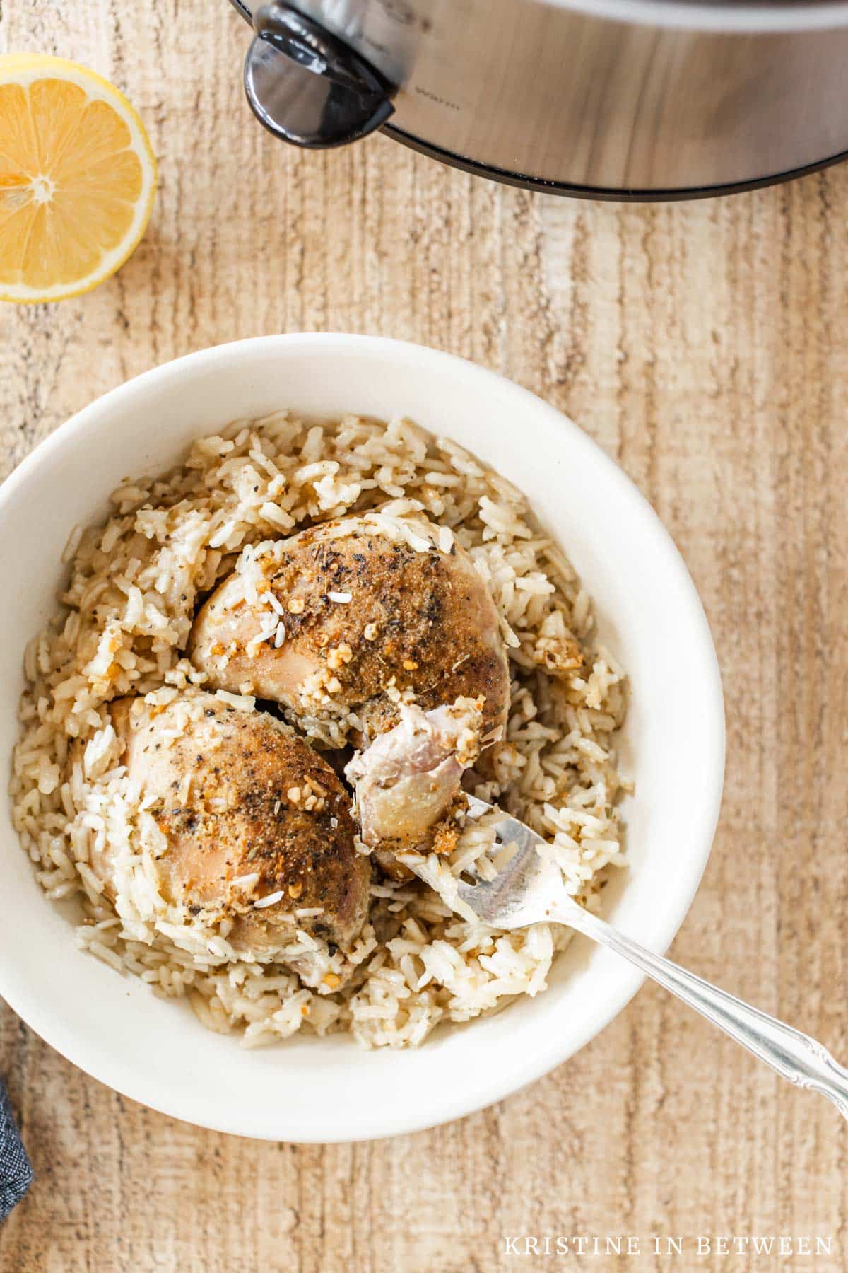 A bite of chicken on a fork sitting in a bowl of cooked chicken thighs and rice.