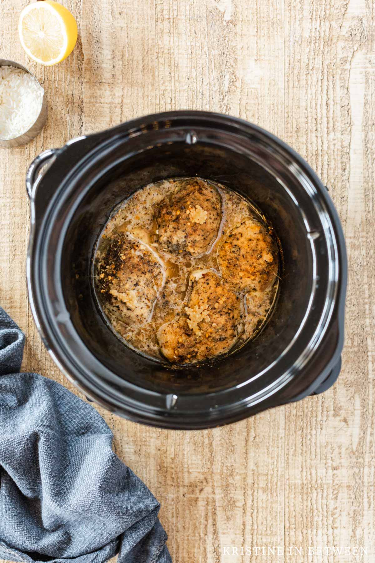 Cooked chicken thighs in a Crock-pot with garlic on top.
