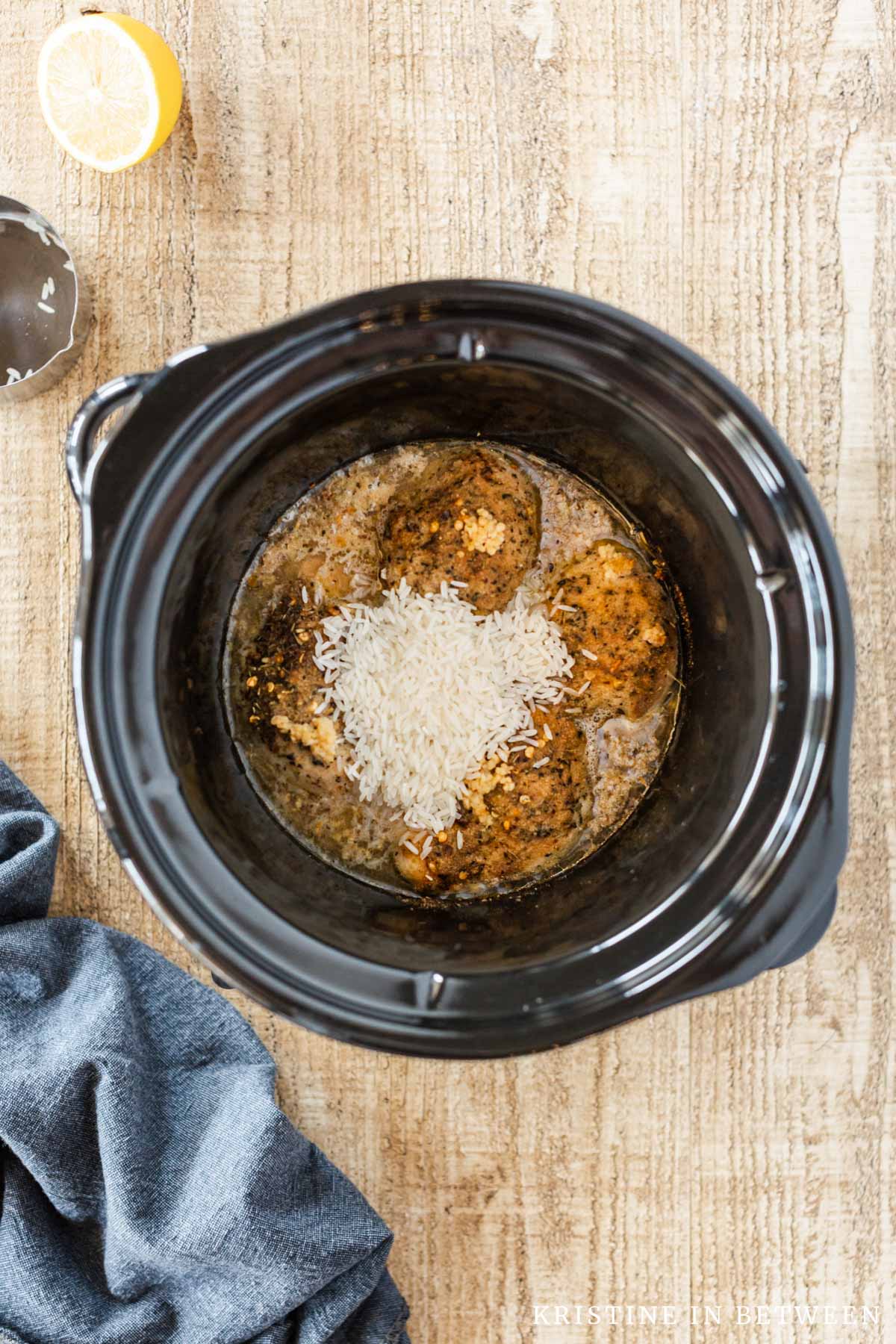 Rice added to cooked chicken thighs in a Crock-pot.