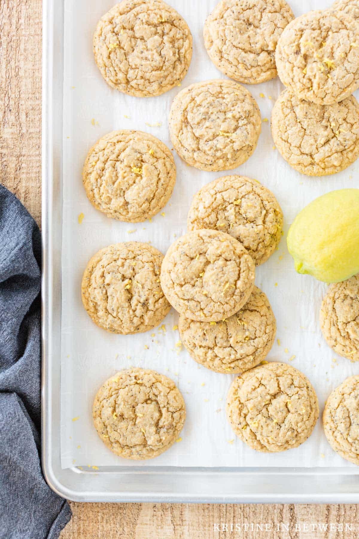 Lemon poppy seed cookies on a baking sheet with a lemon and a blue napkin next to them.