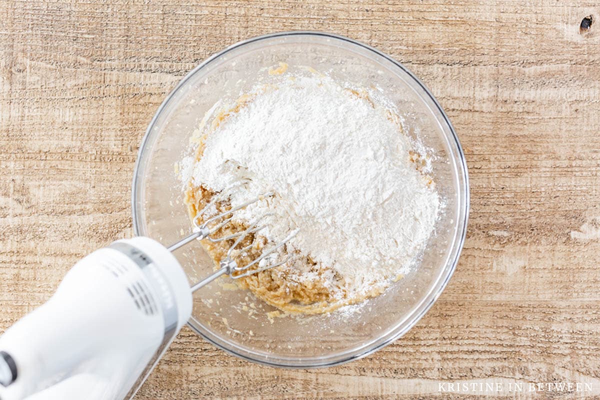 Flour on top of creamed butter and sugar in a glass bowl.