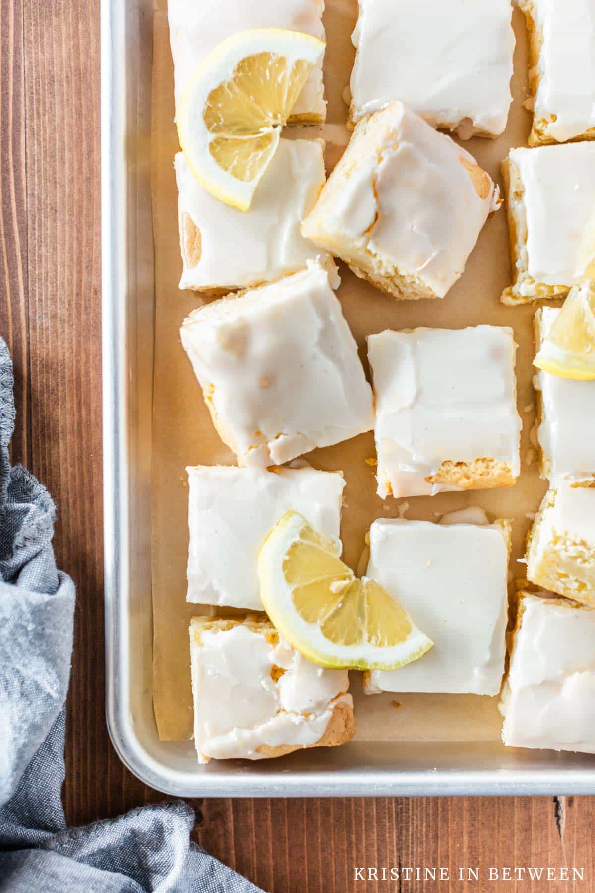 A pan of lemon brownies with lemon slices on top and a blue napkin laying next to them.