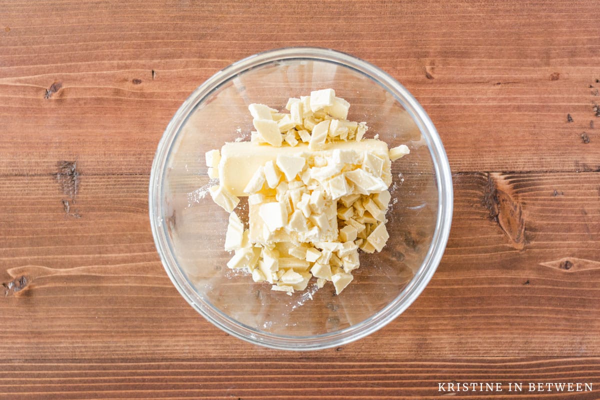 Butter and chopped white chocolate in a glass bowl with a spoon.