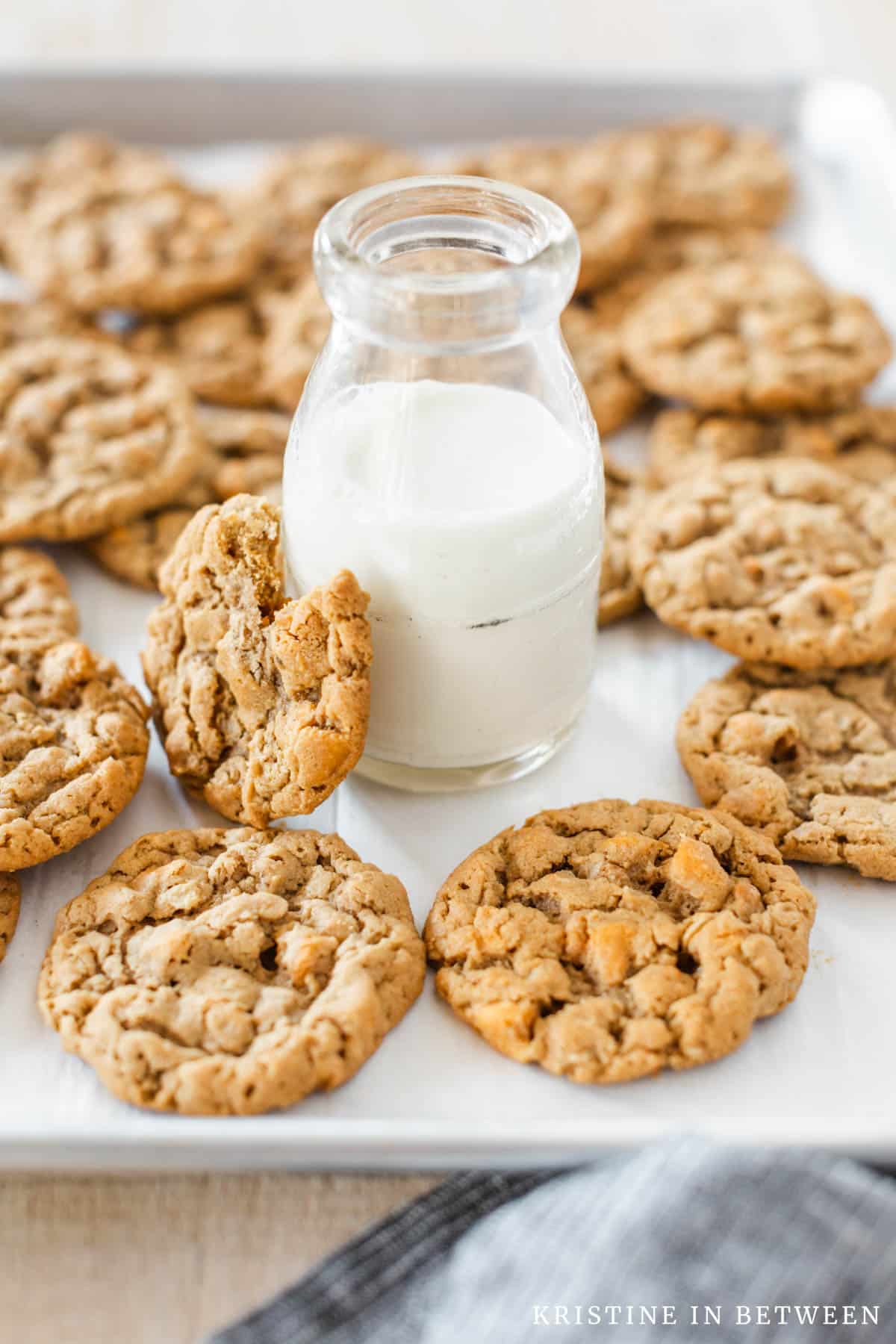 A crinkle topped cookie leaning up on a jar of milk with the rest of the cookies in the background.