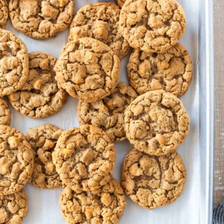 Peanut butter oatmeal butterscotch cookies laying on a baking sheet with a striped napkin next to them.