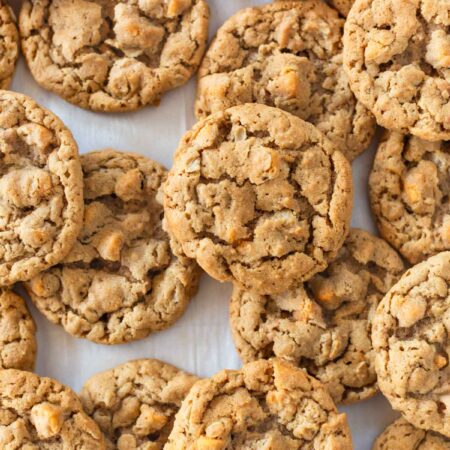 Peanut butter oatmeal butterscotch cookies laying on a baking sheet with a striped napkin next to them.