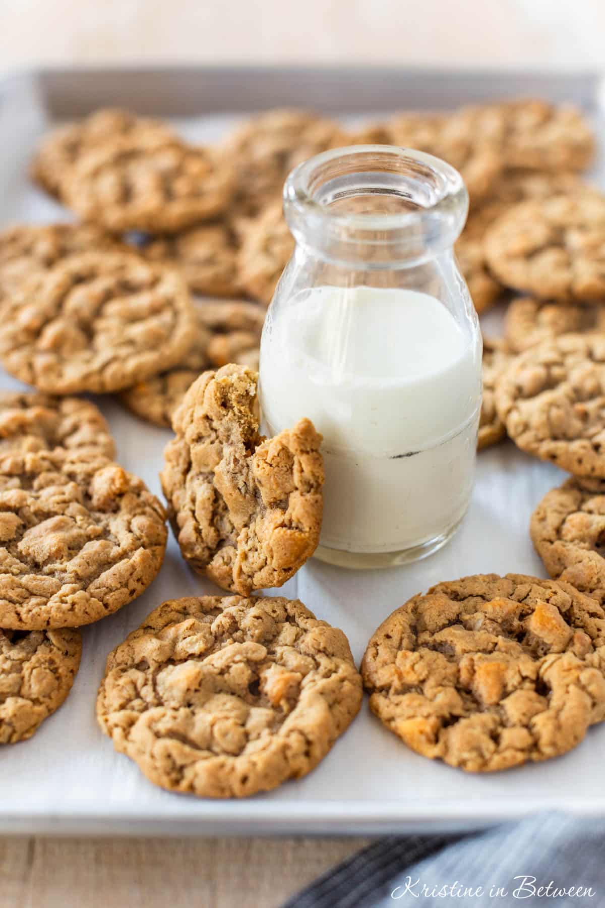 Peanut butter oatmeal butterscotch cookies laying on a baking sheet with a small jar of milk.
