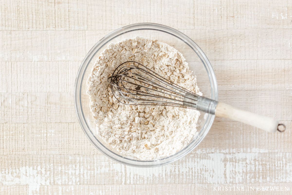 Whisked flour, oats, salt, and baking soda in a glass bowl with a whisk.