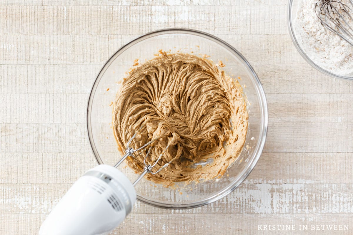 Creamed butter, peanut butter, sugar, and brown sugar in a glass bowl with a mixer.