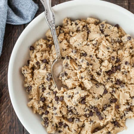 A bowl of chocolate chip edible cookie dough with a spoon in it.