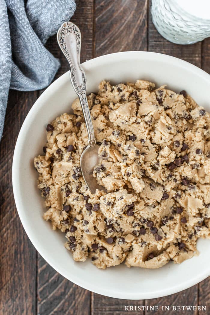 A bowl of chocolate chip edible cookie dough with a spoon in it.