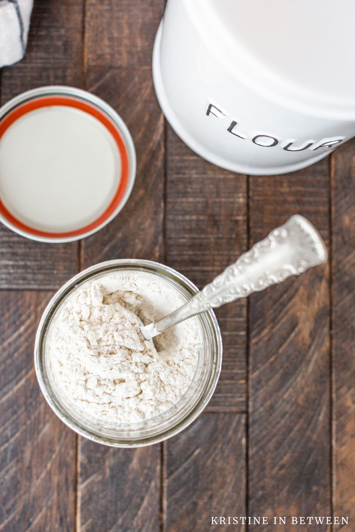 A mason jar with flour inside and a canister of flour in the background.