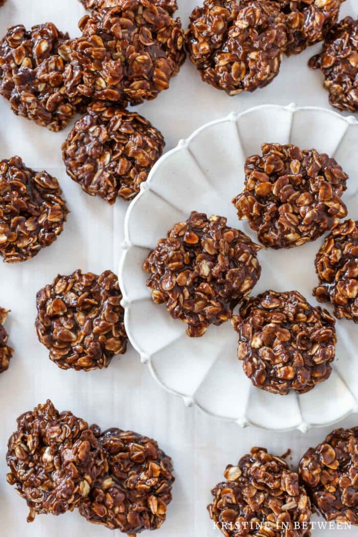 Chocolate and peanut butter no-bake cookies sitting on a baking tray with a few on a white scalloped plate.