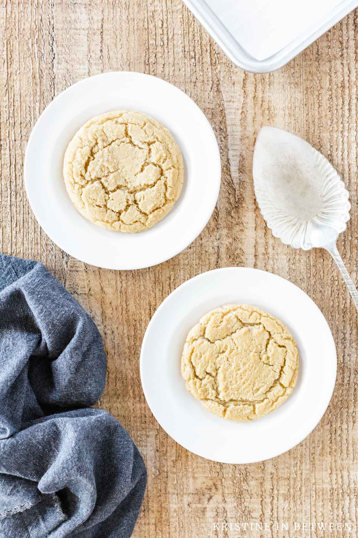 Two sugar cookies sitting on white plates with a blue napkin next to them.