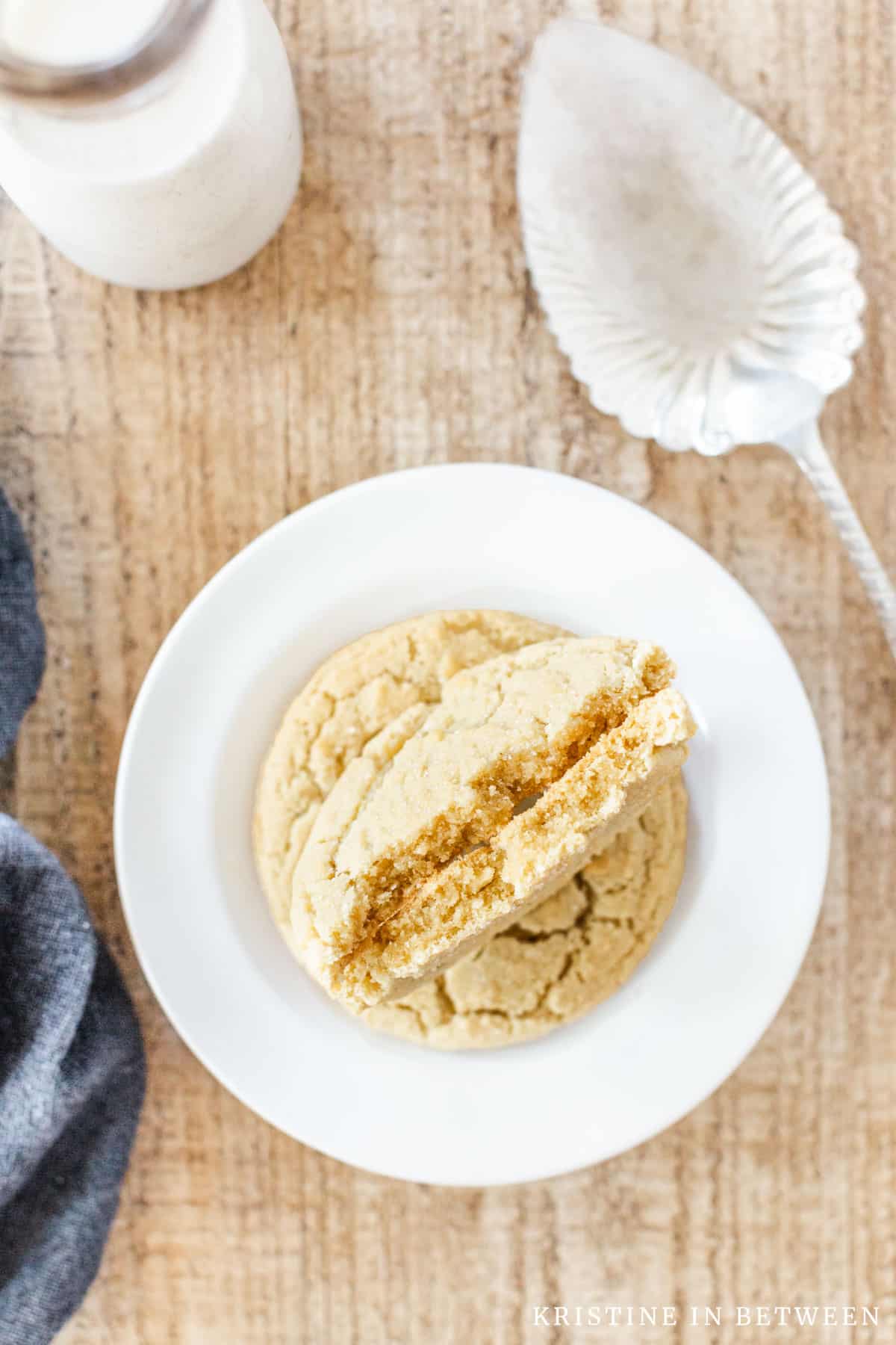 A sugar cookie broken in half to show the detail sitting on a white plate with a jar of milk in the background.