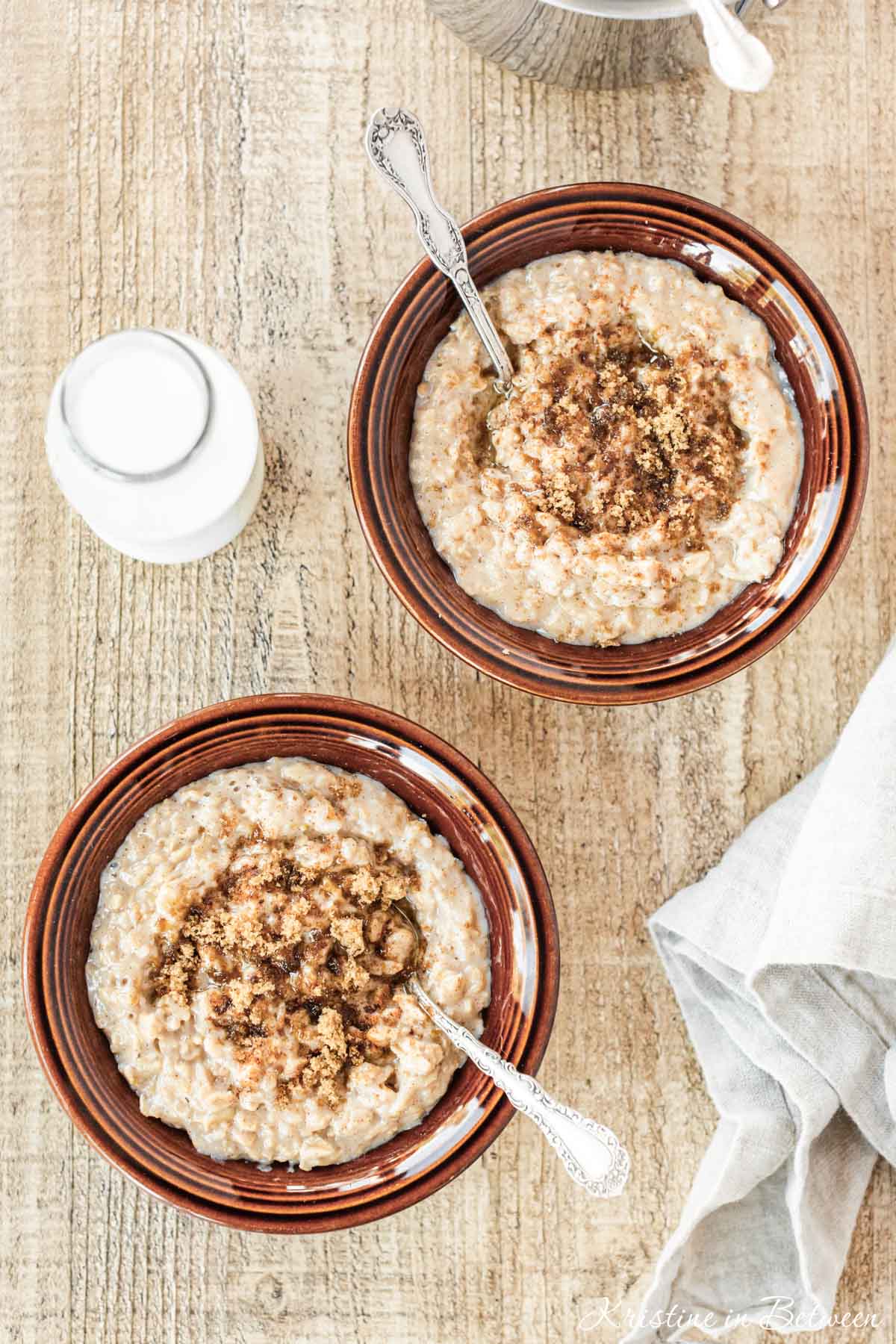 Two bowls of brown sugar cinnamon oatmeal with spoons, topped with brown sugar and cinnamon.