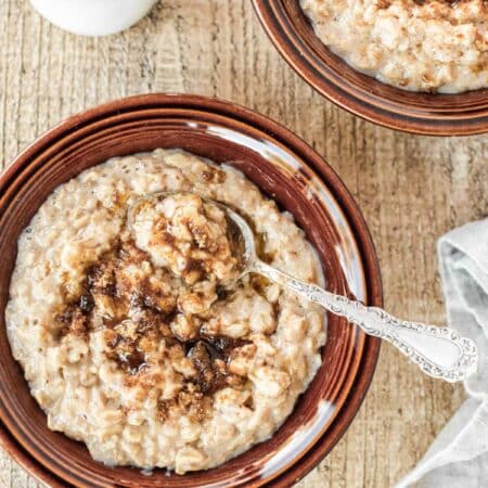 Two bowls of cooked oatmeal with spoons, topped with brown sugar and cinnamon.