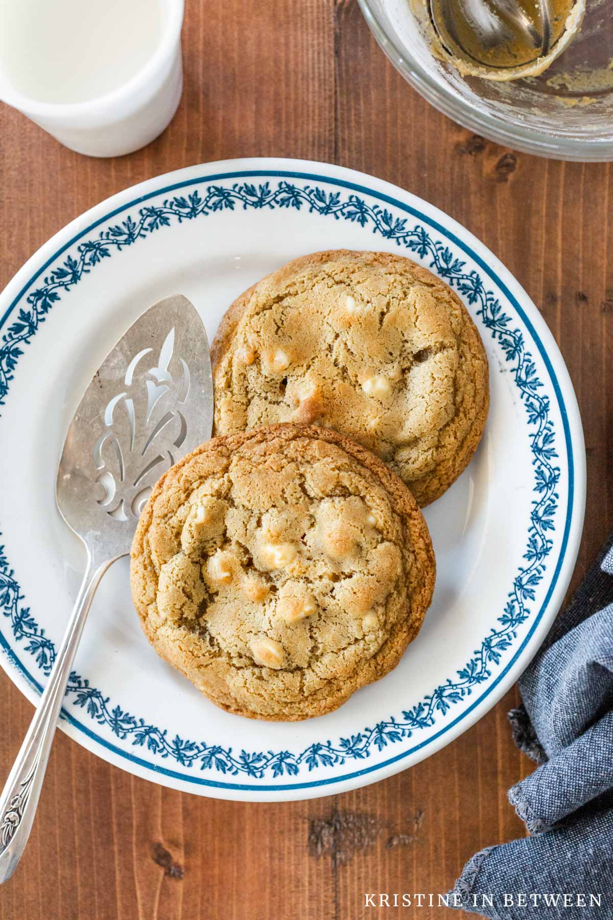 Two macadamia nut cookies sitting on a plate with a blue border and an antique spatula.