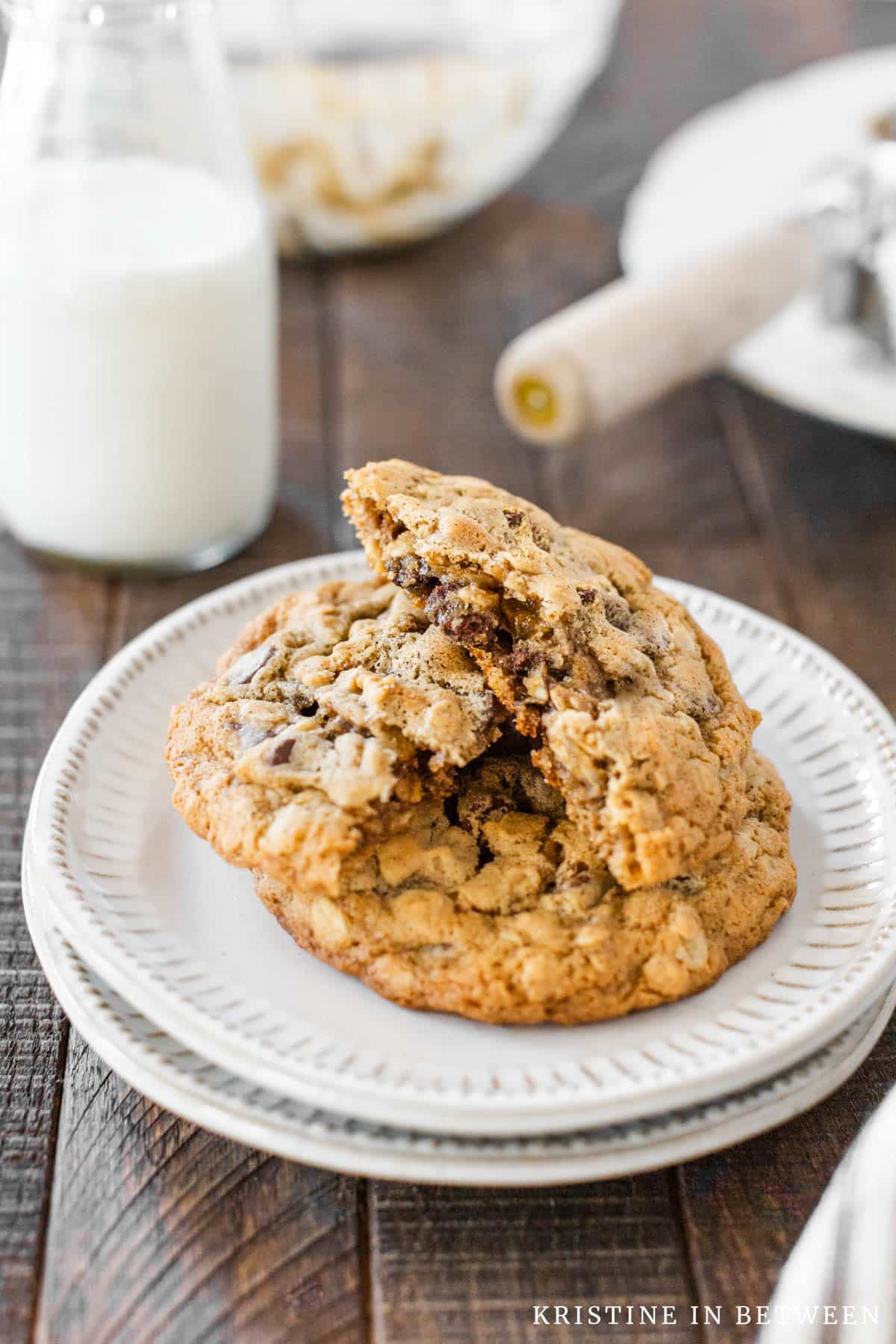 Two oatmeal cookies stacked up on a white plate, broken in half to show the inside of the cookie.