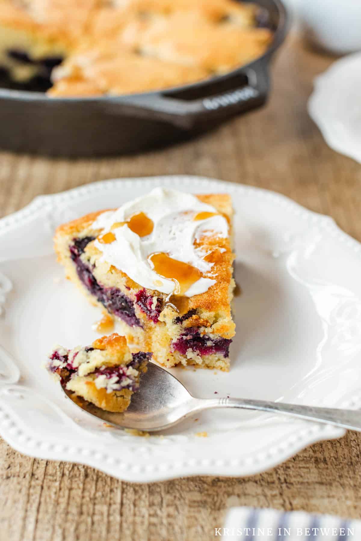 A slice of blueberry cornmeal skillet cake on a white plate with a spoon.