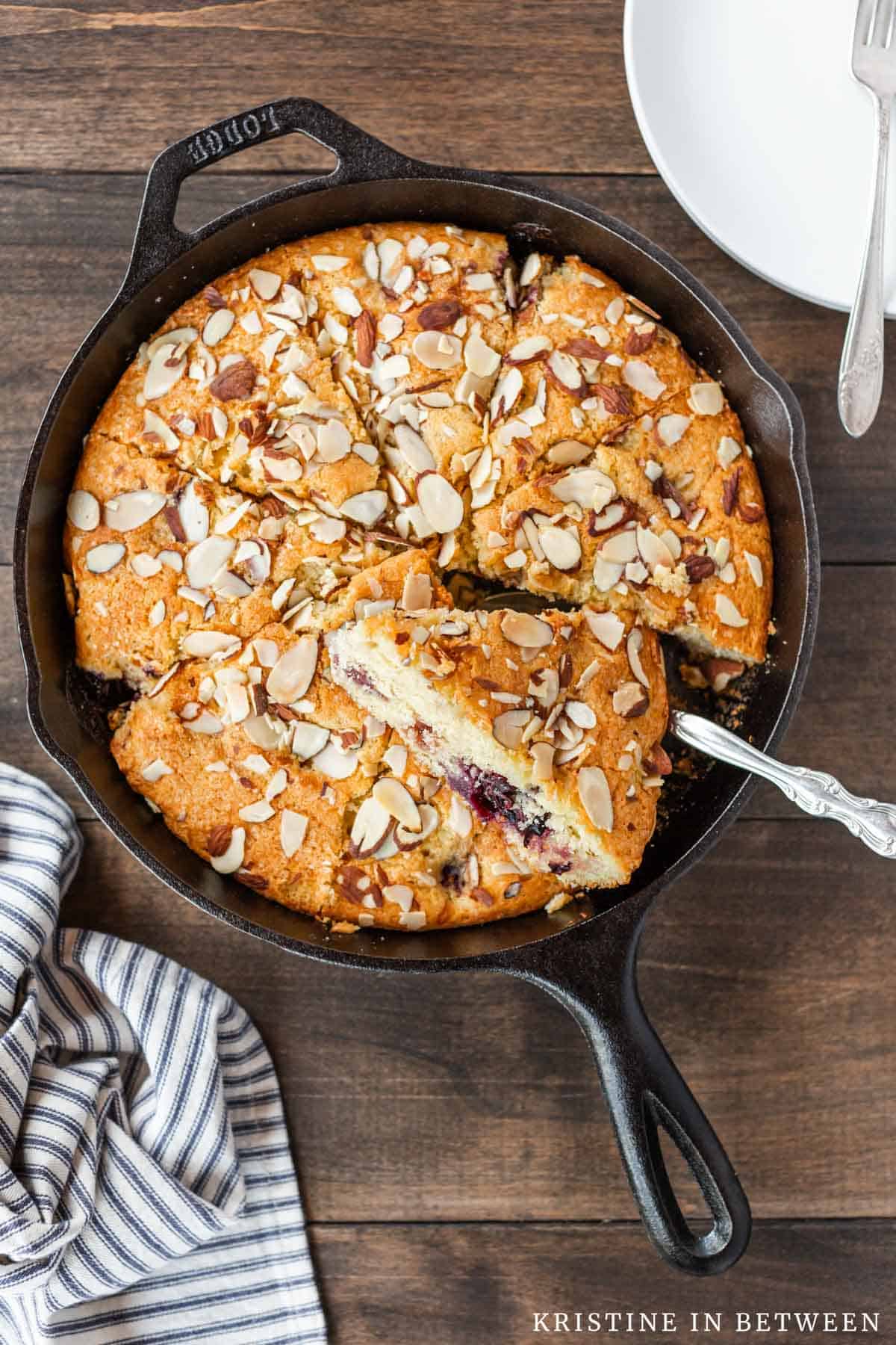 A cherry almond skillet cake in a cast iron skillet with a slice removed.