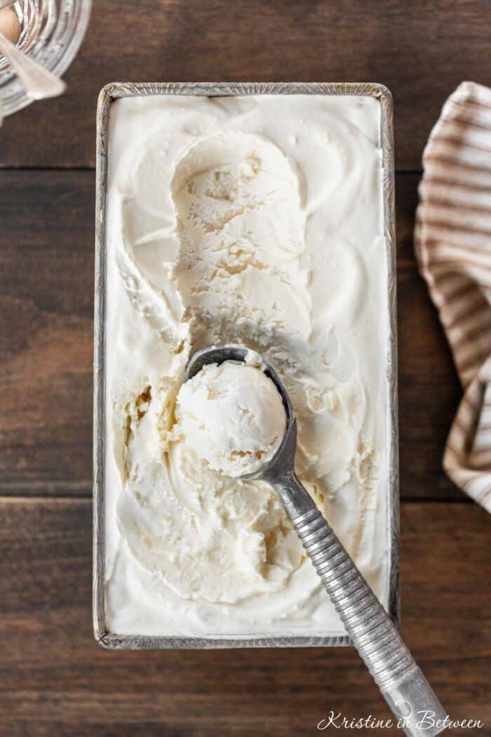 Vanilla no-churn ice cream in a loaf pan with a scoop on top.