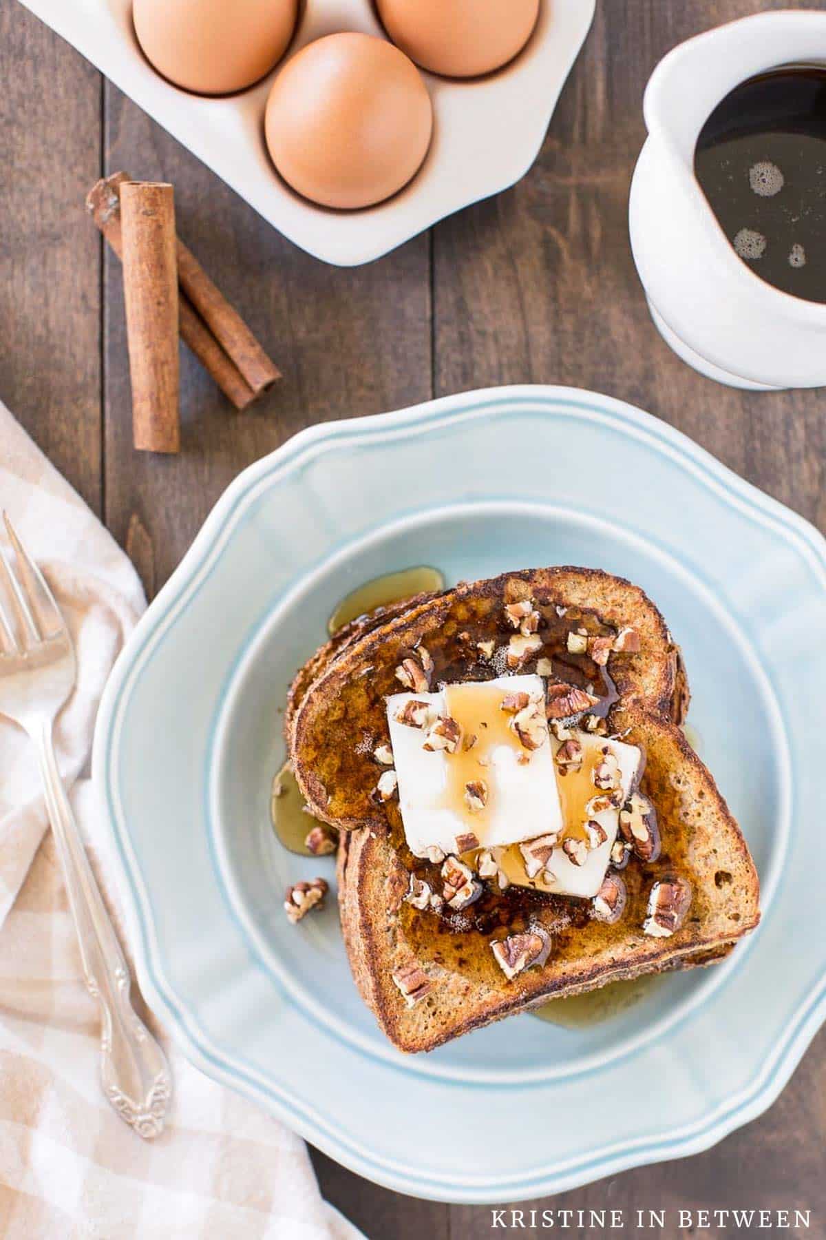 Two slices of pumpkin French toast sitting on a blue plate with butter, syrup, and pecans on top.