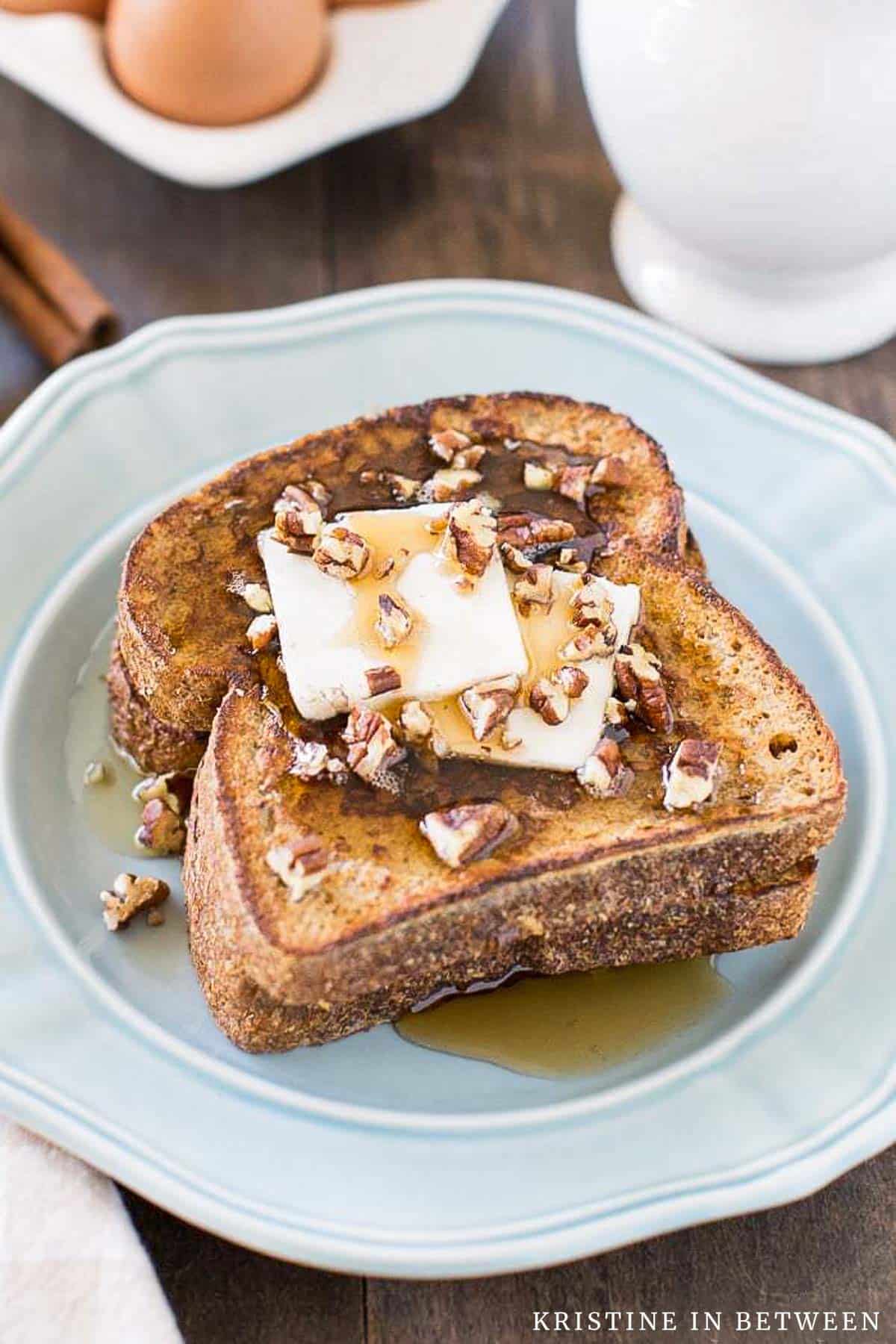 Two slices of pumpkin French toast sitting on a blue plate with butter, syrup, and pecans on top.
