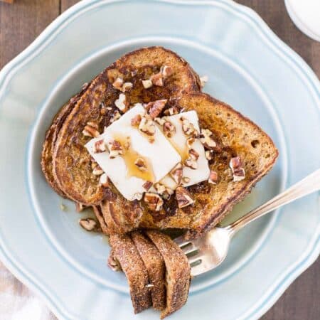 Two slices of pumpkin French toast sitting on a blue plate with butter, syrup, and pecans on top.