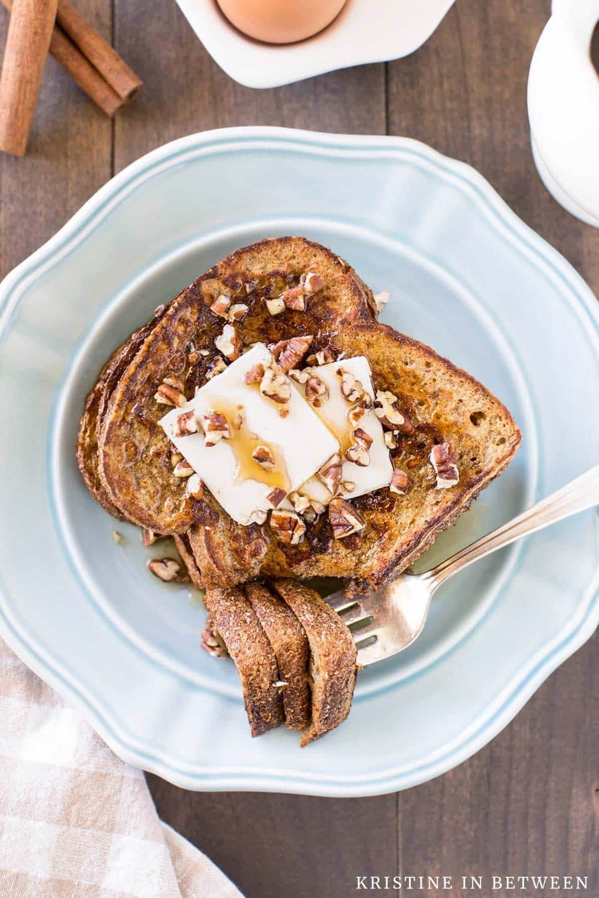 Two slices of pumpkin French toast sitting on a blue plate with butter, syrup, and pecans on top.