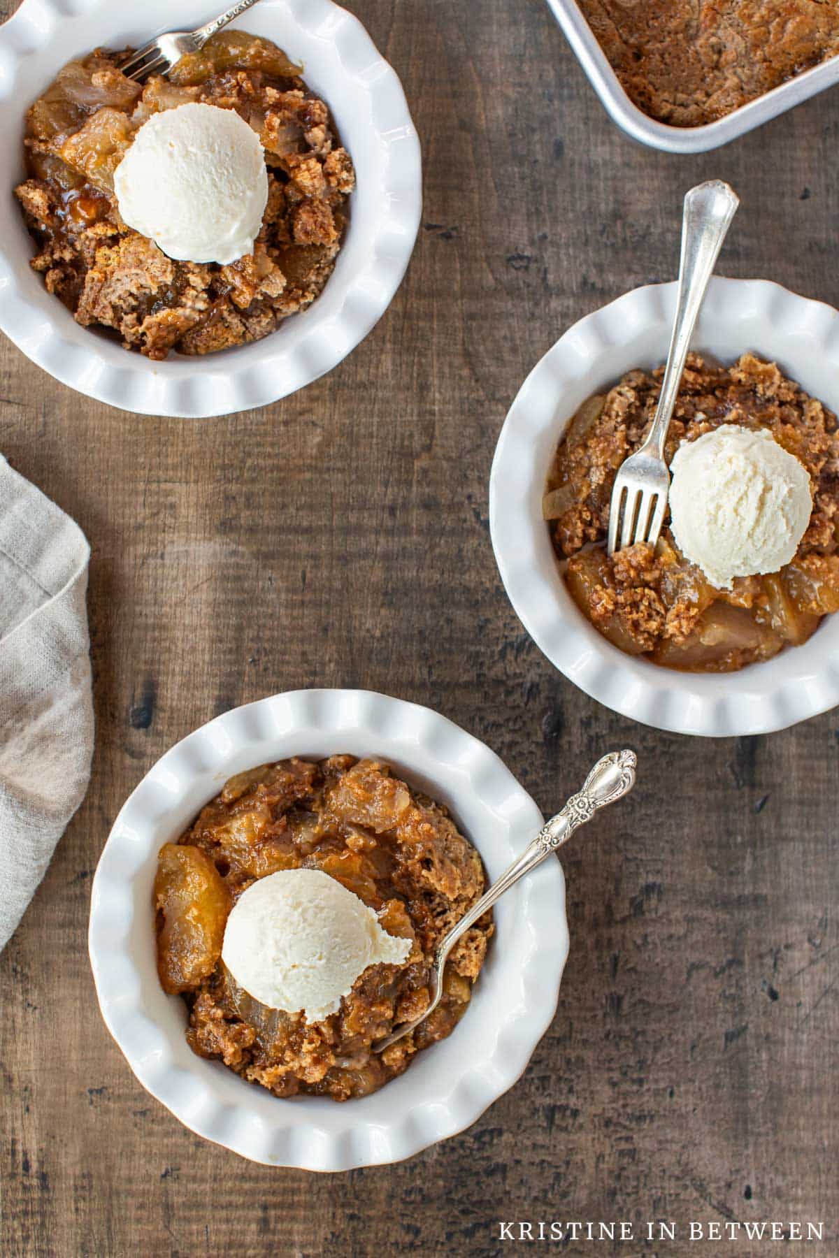 Three bowls of apple pie dump cake with ice cream on top.