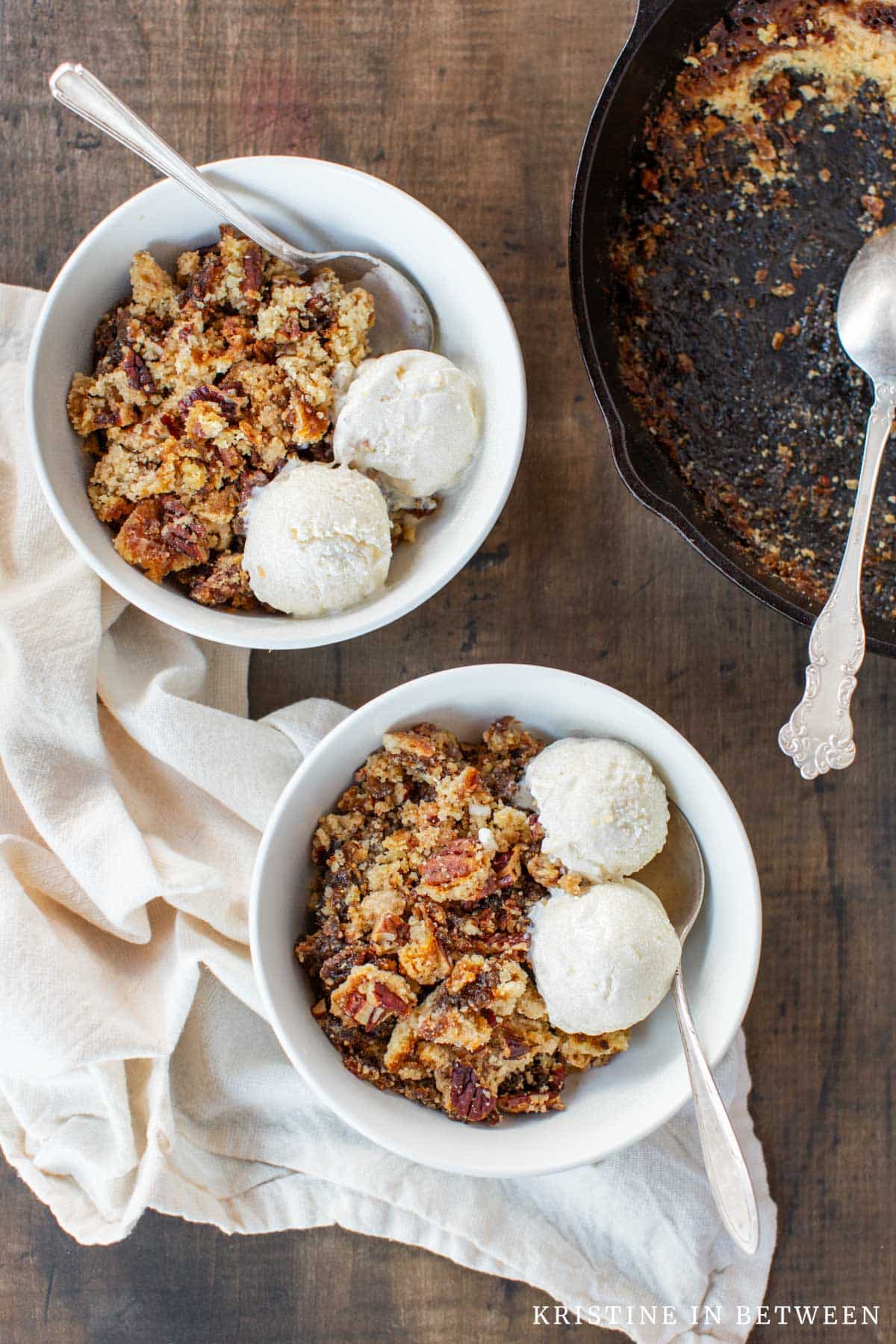 Two bowls of pecan pie dump cake with ice cream and a spoon.