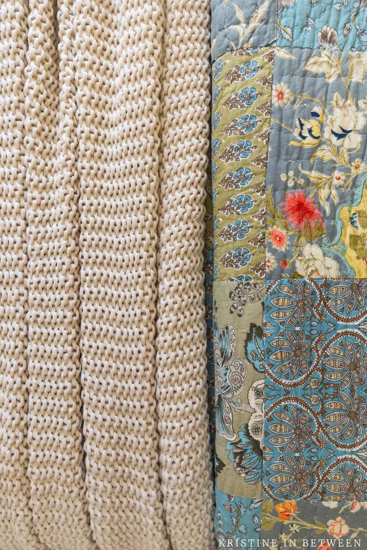 A closeup of layered bedding, a chunky tan blanket and a quilt in blues and greens.