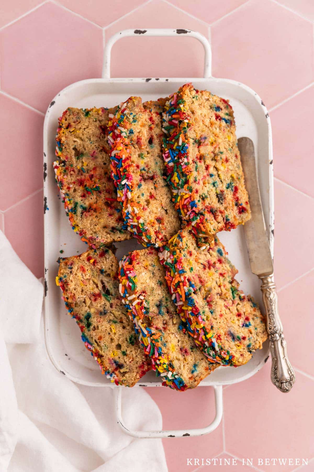 Slices of sugar cookie banana bread laying on a white tray with a white napkin and an antique knife.
