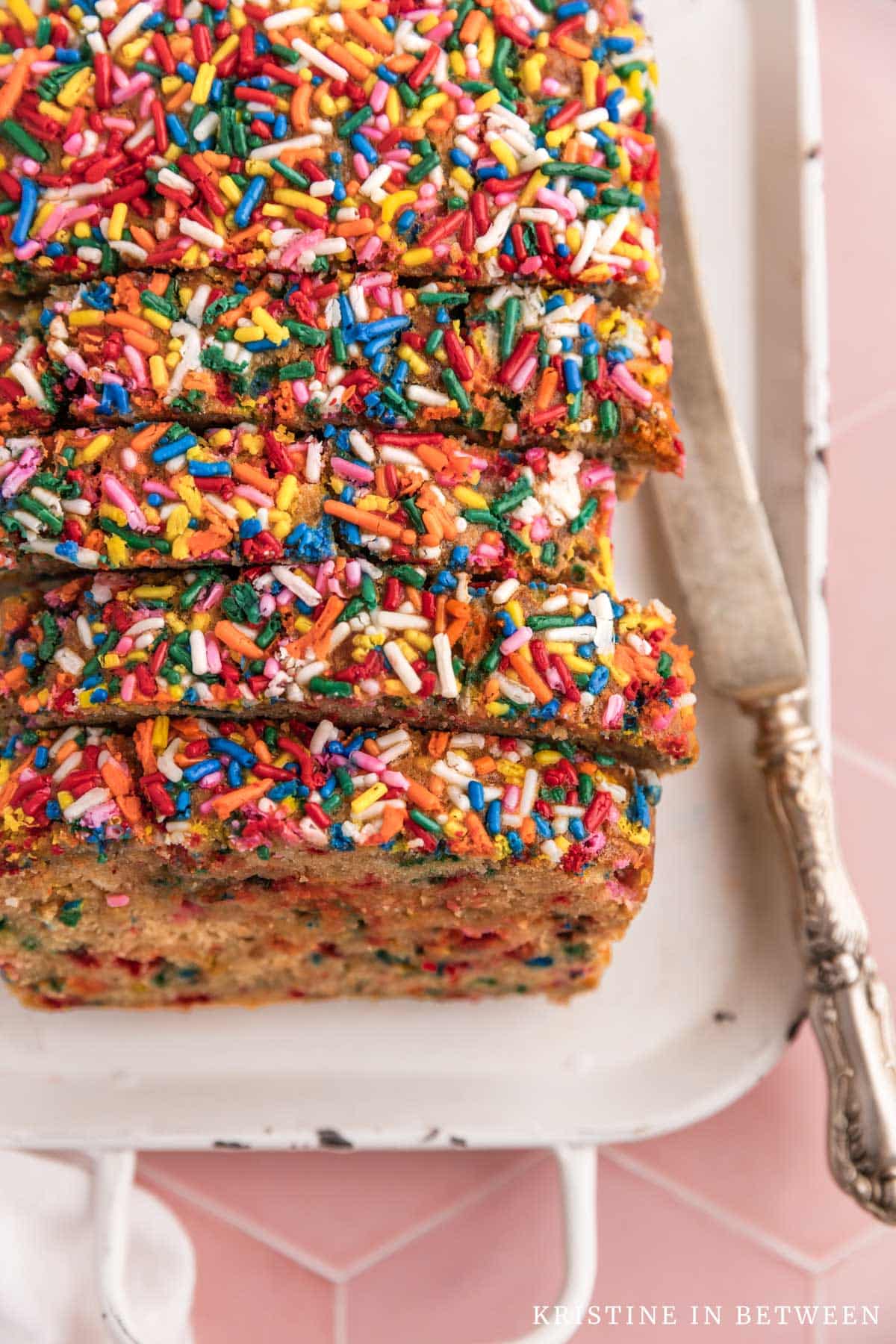 Slices of banana bread with sprinkles on top sitting on a white tray with an antique knife.