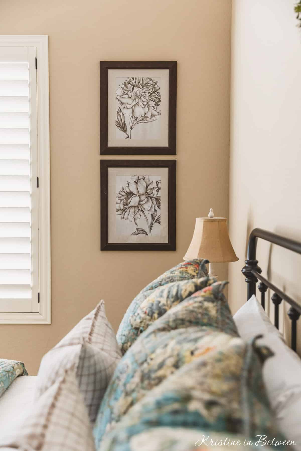 A guest bedroom with blue quilted bedding, a metal bed, and some floral artwork on the wall.