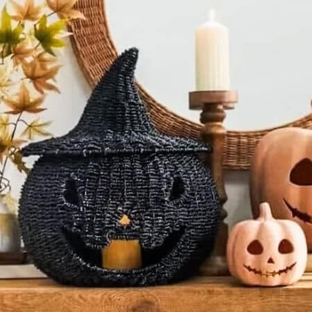 A black seagrass pumpkin sitting on a mantel with two smaller pumpkins and a pillar candle.