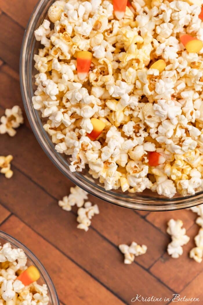 Popcorn and candy corn in glass bowls with some popcorn scattered around.