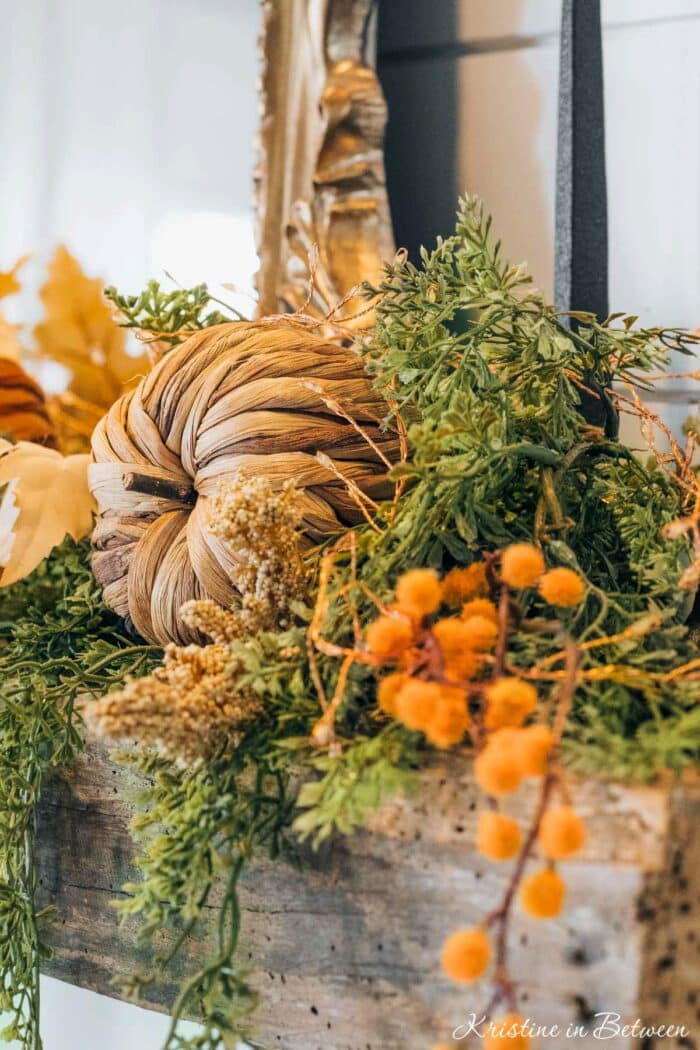 A wooden mantle decorated with fall foliage and whicker pumpkins.