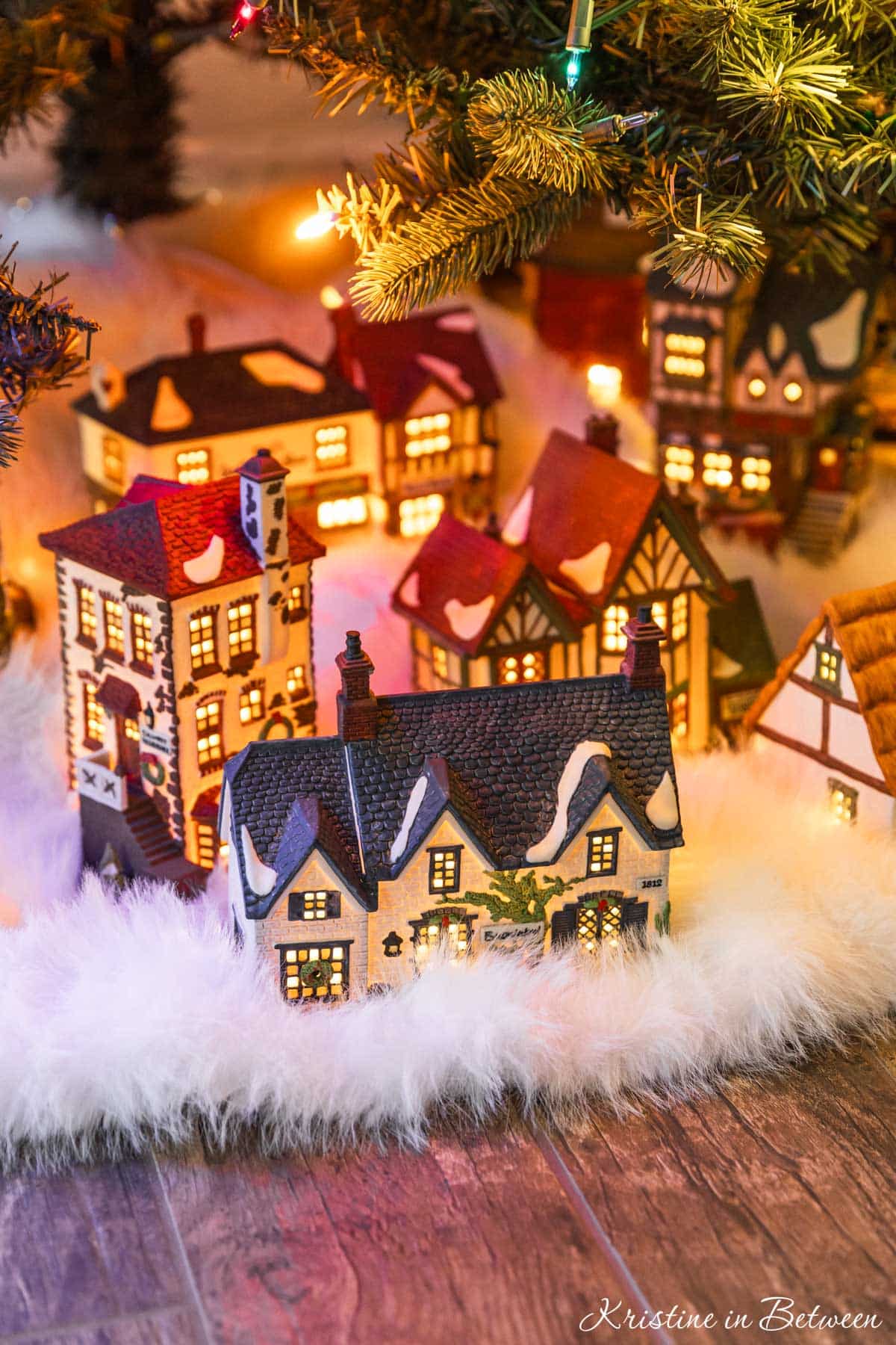 A glowing vintage Christmas village on a white tree skirt under a Christmas tree.