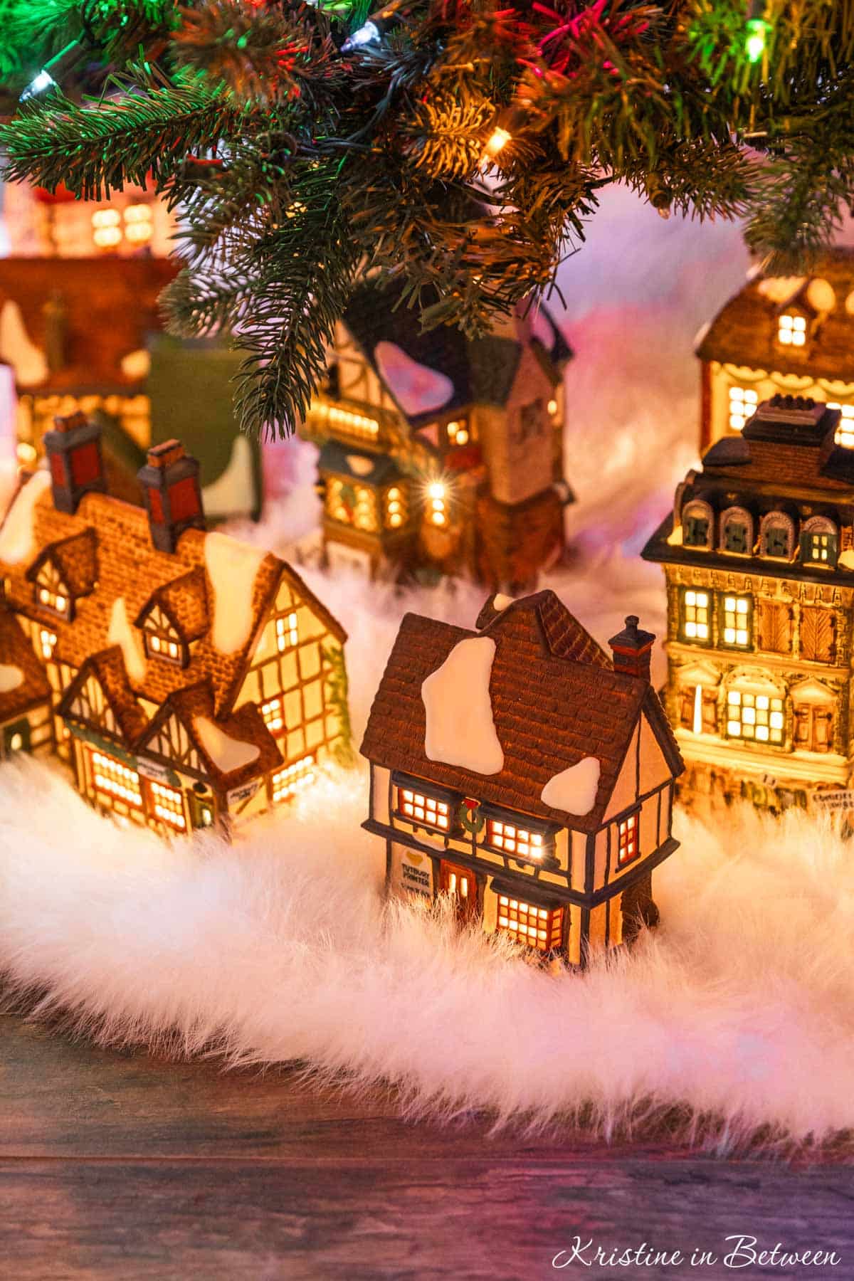 A glowing vintage Christmas village on a white tree skirt under a Christmas tree.