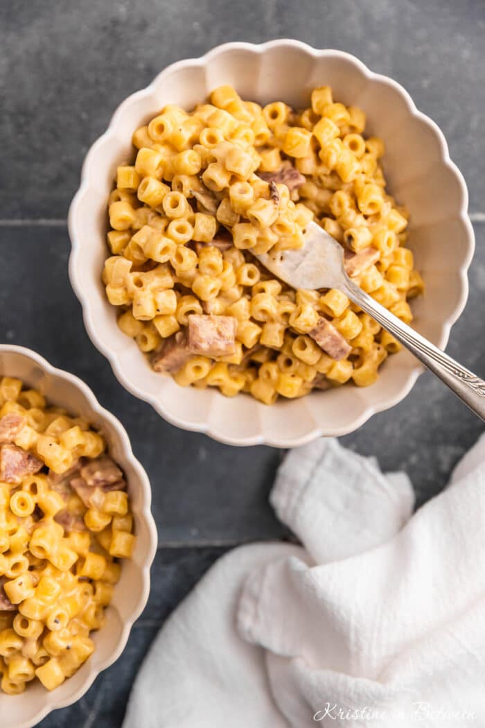Two bowls of homemade macaroni and cheese with a fork and white linen napkin.