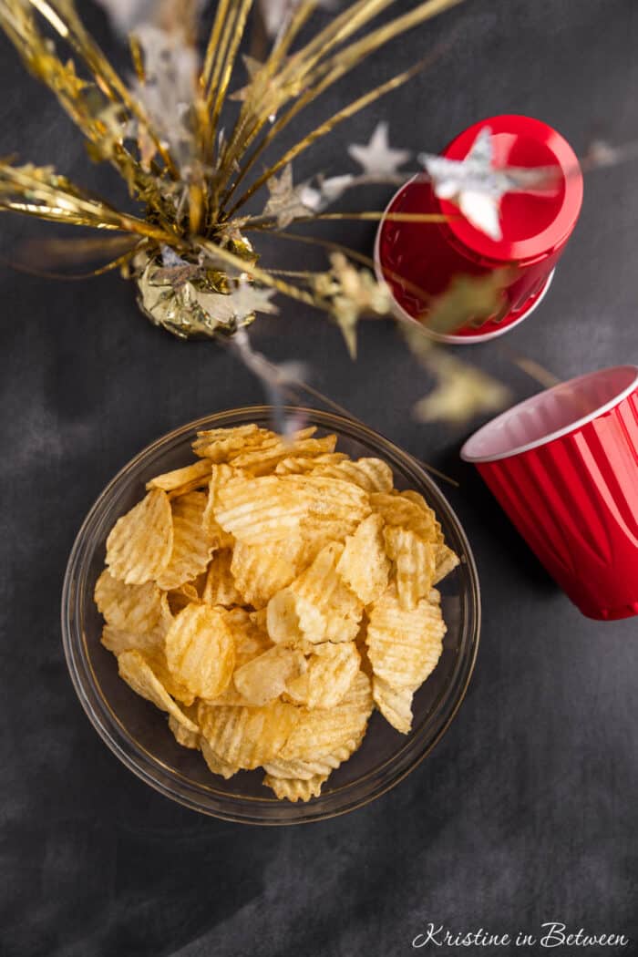 A glass bowl with potato chips in it and red Solo cups sitting next to it.