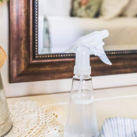 A spray bottle of old-fashioned glass cleaner sitting on a dresser next to a doily.