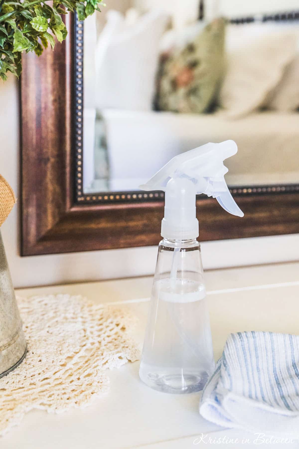 A spray bottle of old-fashioned glass cleaner sitting on a dresser next to a doily.
