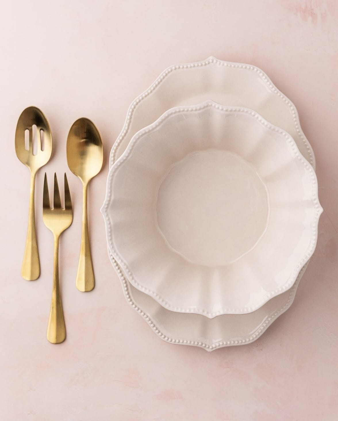 Serving dishes with gold silverware on a pink background.